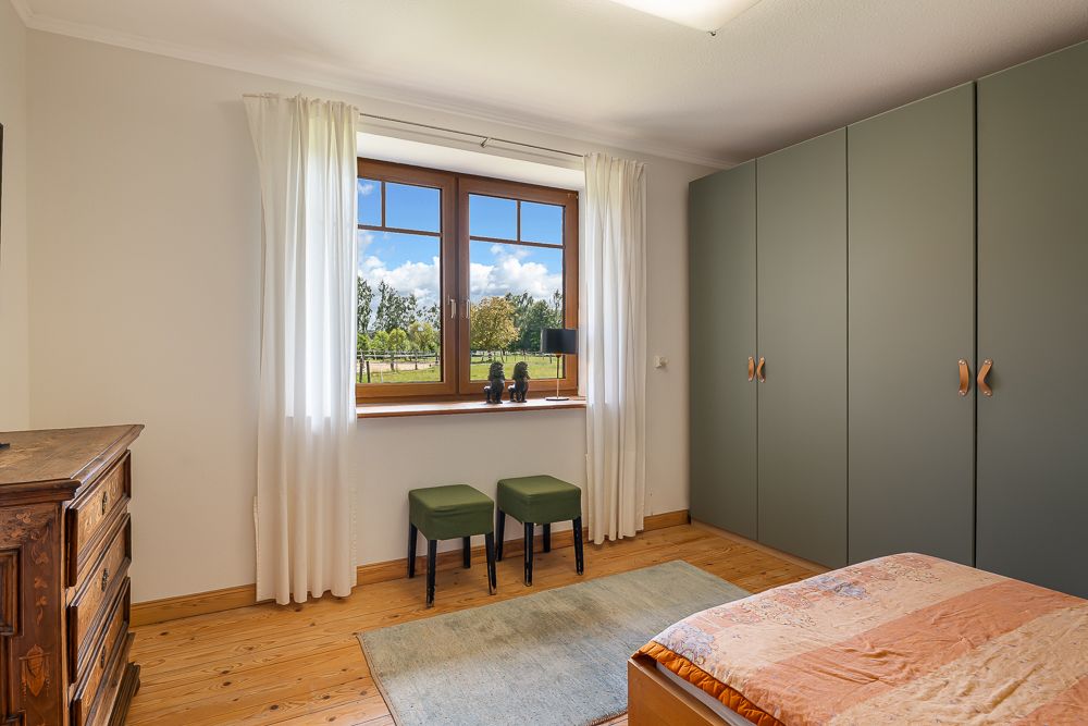 Helles Schlafzimmer mit großem Fenster, grünem Schrank und Holzboden.