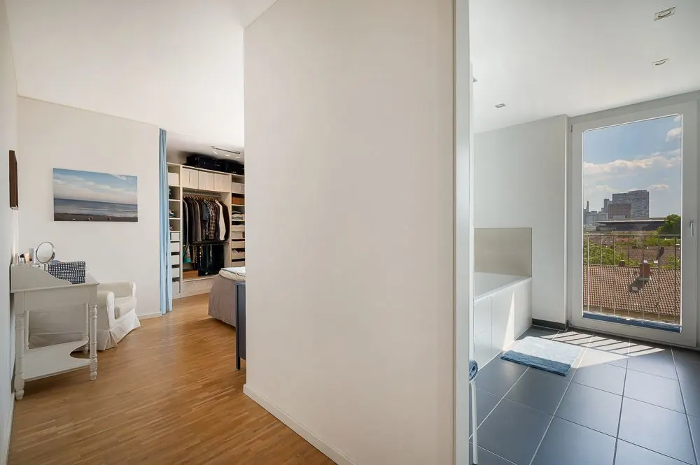 Flur mit Blick in ein Schlafzimmer mit Ankleide und in ein helles Bad mit großem Fenster.