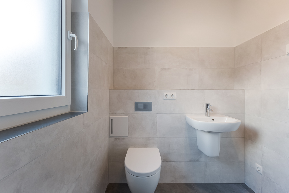 Modernes Badezimmer mit wandhängender Toilette, kleinem Waschbecken und Fenster.