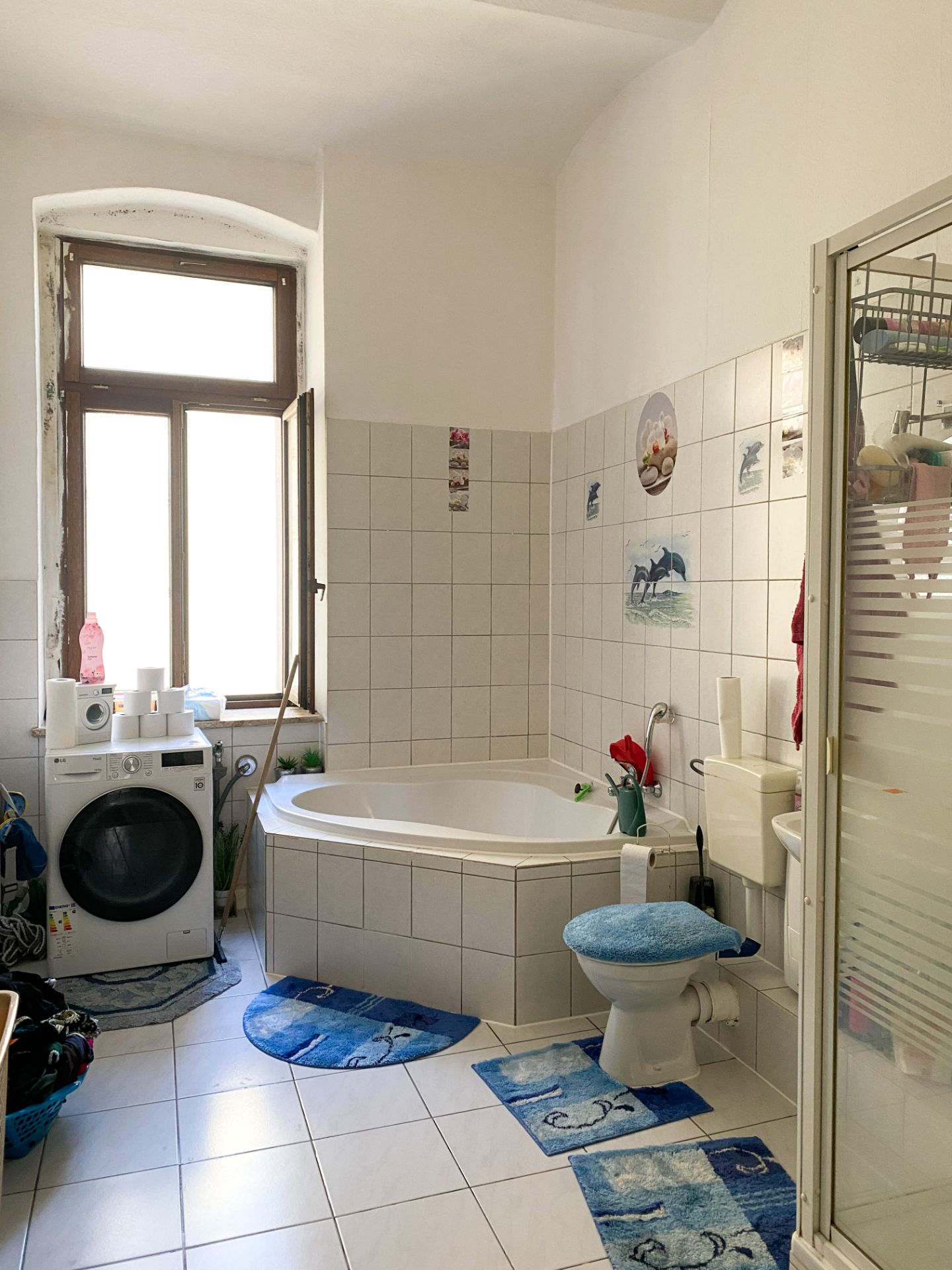 Helles Badezimmer mit Eckbadewanne, Waschmaschine, WC und bunten blauen Teppichen.