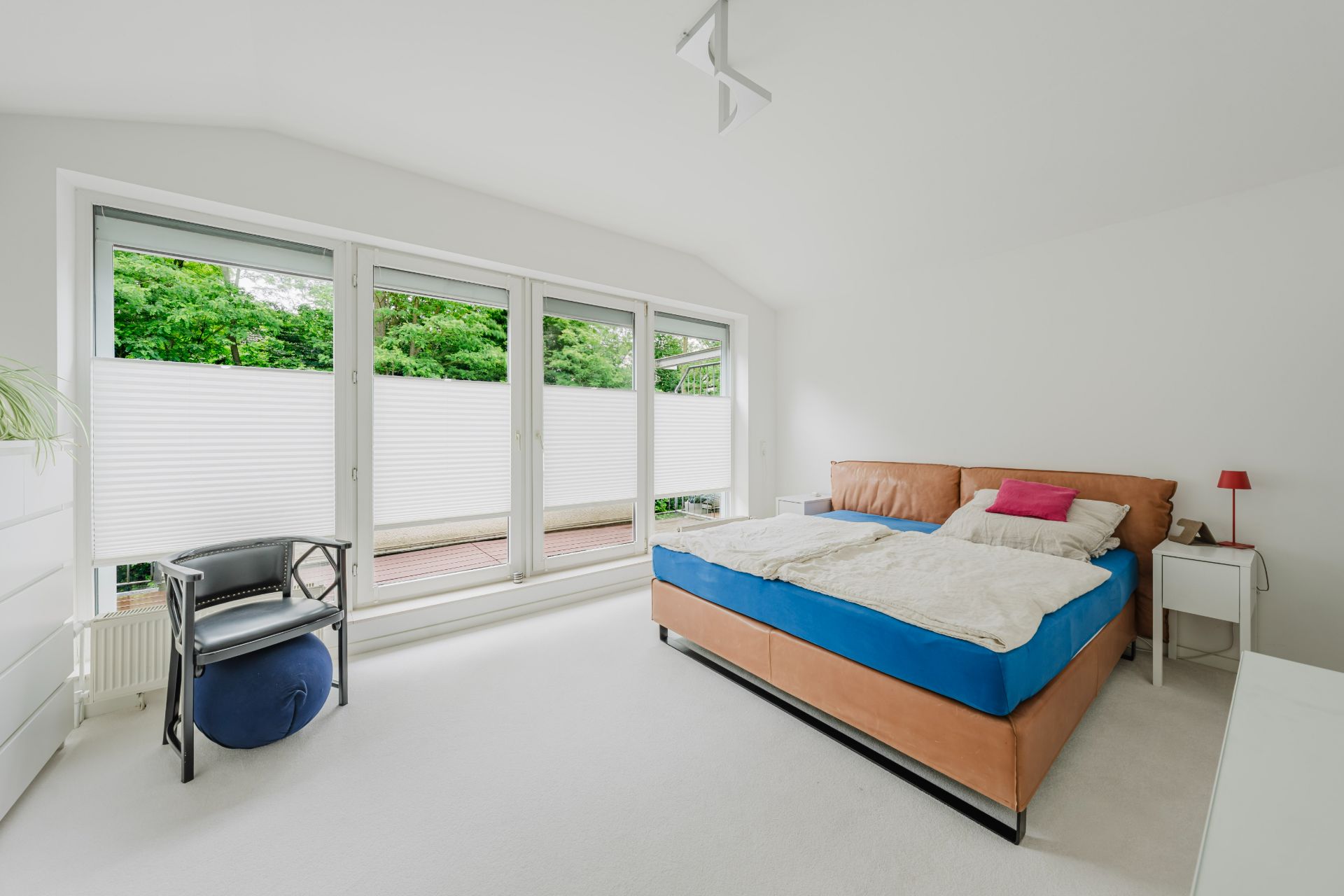 Helles Schlafzimmer mit großem Bett, weißen Wänden und bodentiefen Fenstern mit Blick ins Grüne.