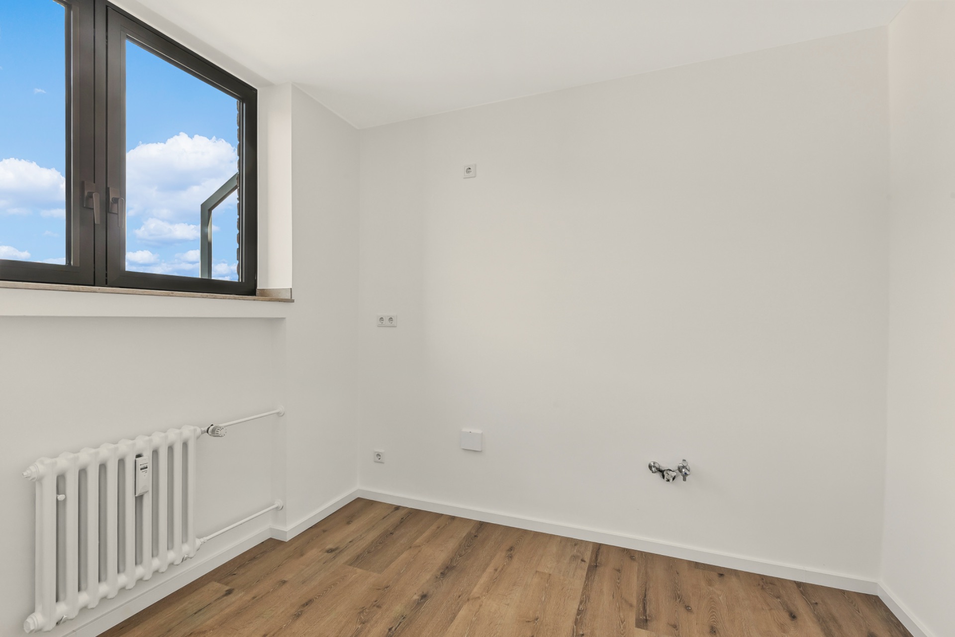 Heller, leerer Raum mit Holzfußboden, weißer Wand, Fenster und Heizkörper.