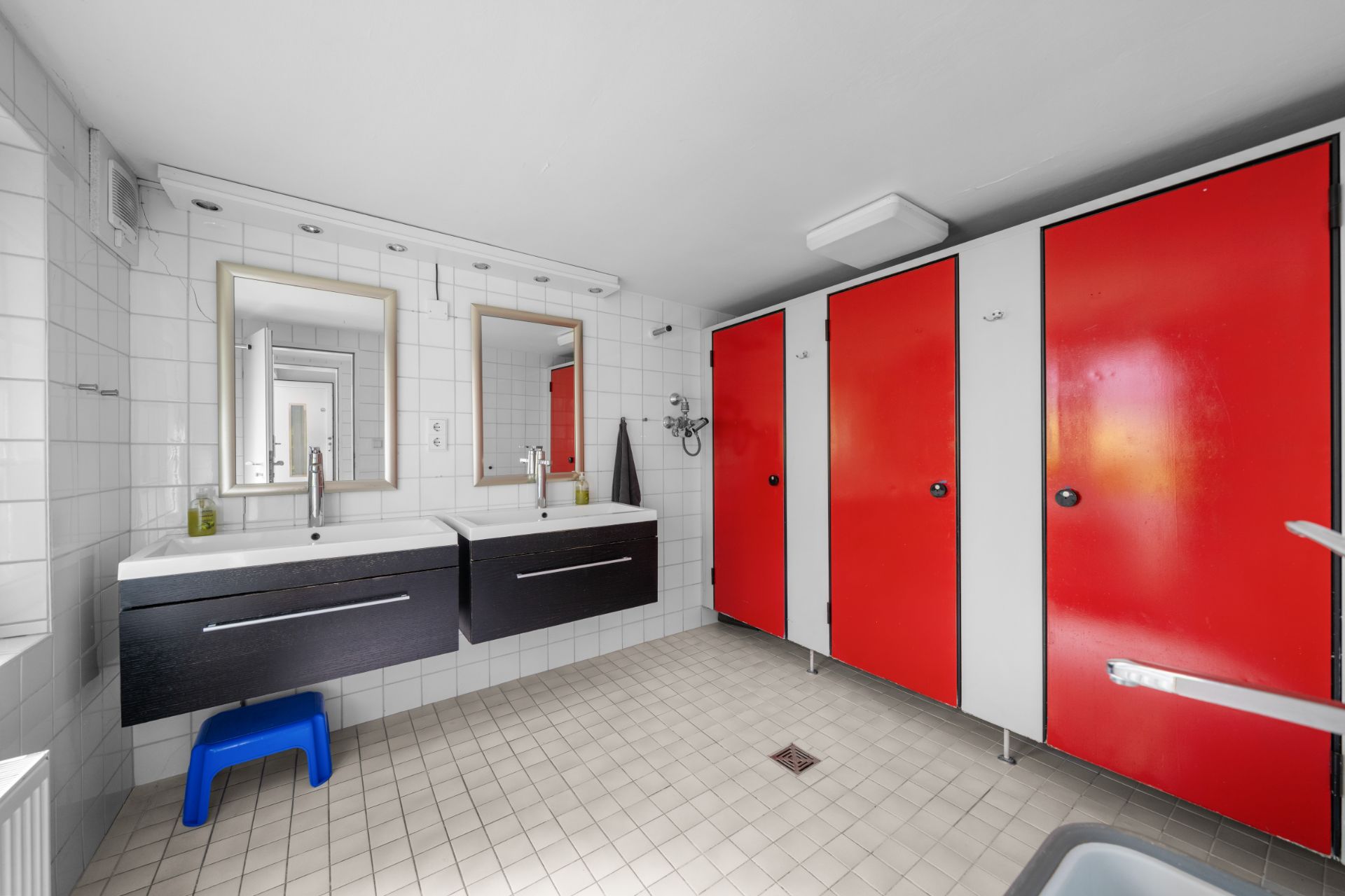 Badezimmer mit zwei Waschbecken, Spiegeln und drei roten Kabinentüren.