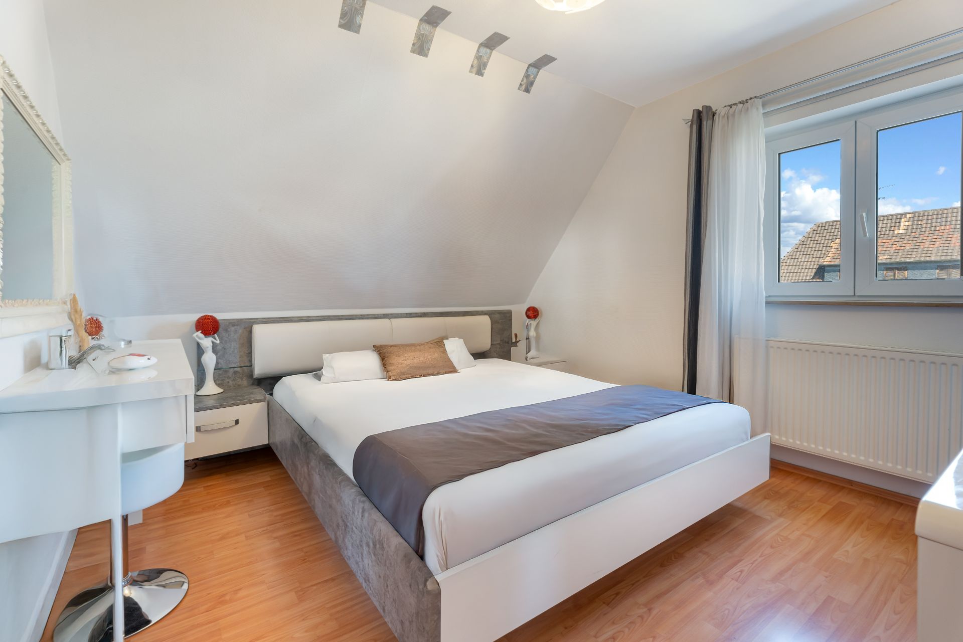 Modernes Schlafzimmer mit großem Bett, Schreibtisch, Holzfußboden und Fenster mit Vorhängen.