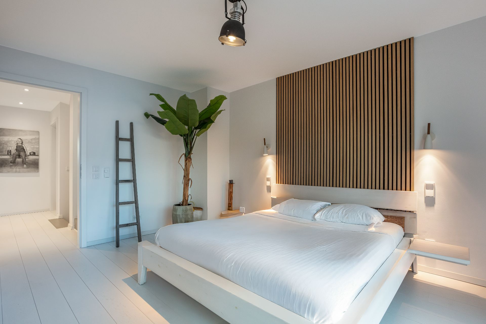 Modernes Schlafzimmer mit großem Bett, Holzpaneelwand, Pflanze und Leiter als Dekoration.