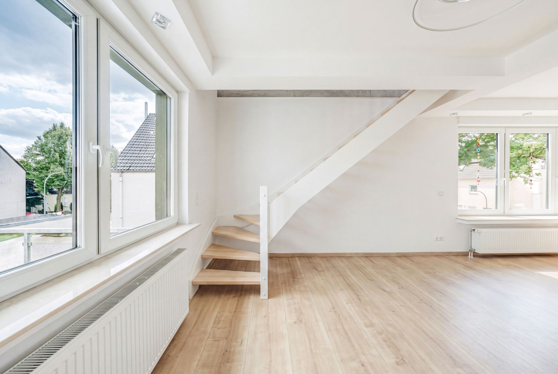 Helles Wohnzimmer mit großem Fenster, Holzboden und moderner Treppe.