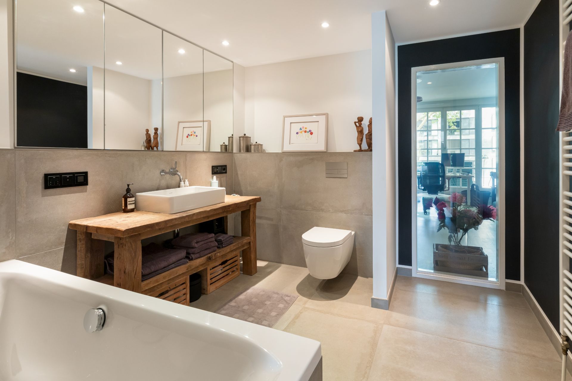 Modernes Badezimmer mit Badewanne, Waschbecken auf Holztisch, WC und großem Spiegel.
