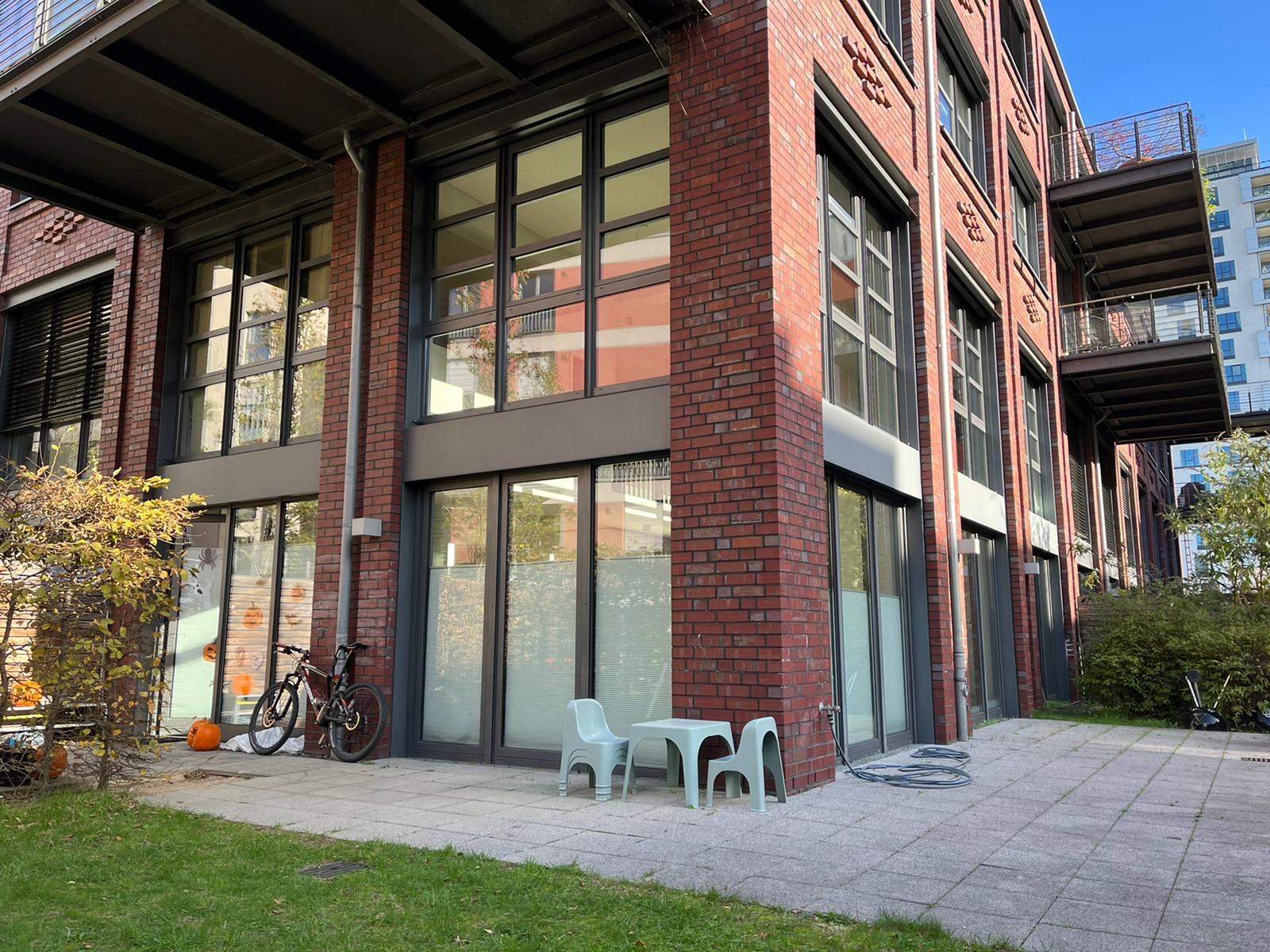 Backsteinhaus mit großen Fenstern, Terrasse mit Tisch, zwei Stühlen und Fahrrad.