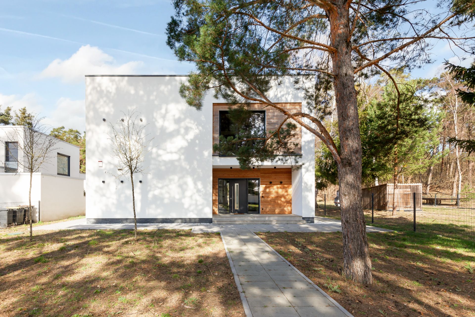 Modernes weißes Wohnhaus mit großen Fenstern und flachem Dach, vor dem ein Baum steht.