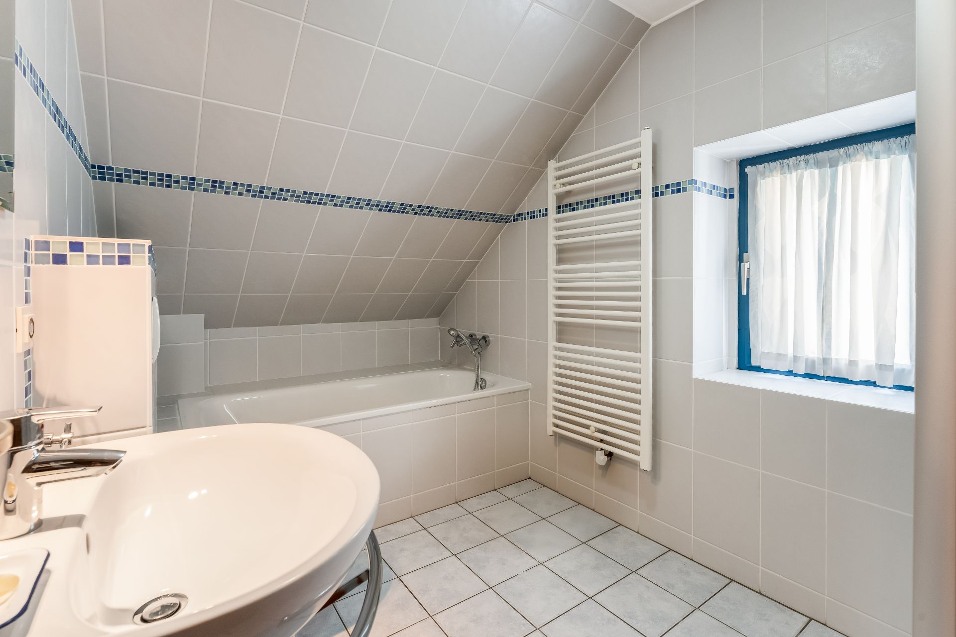 Modernes Bad mit Waschbecken, Badewanne, Fenster und Handtuchheizkörper unter schrägem Dach.