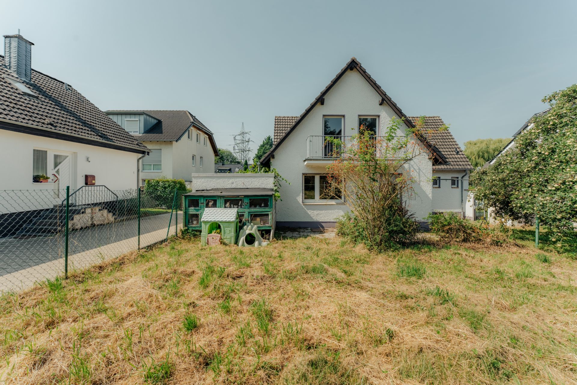 Garten mit grünem Rasen, Hasenstall und Blick auf ein Einfamilienhaus mit Satteldach.