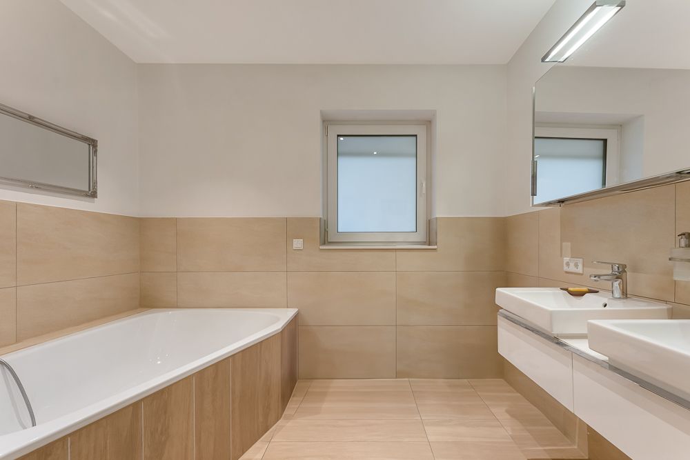 Modernes Badezimmer mit Badewanne, Doppelwaschbecken, Fenster und großem Spiegel.