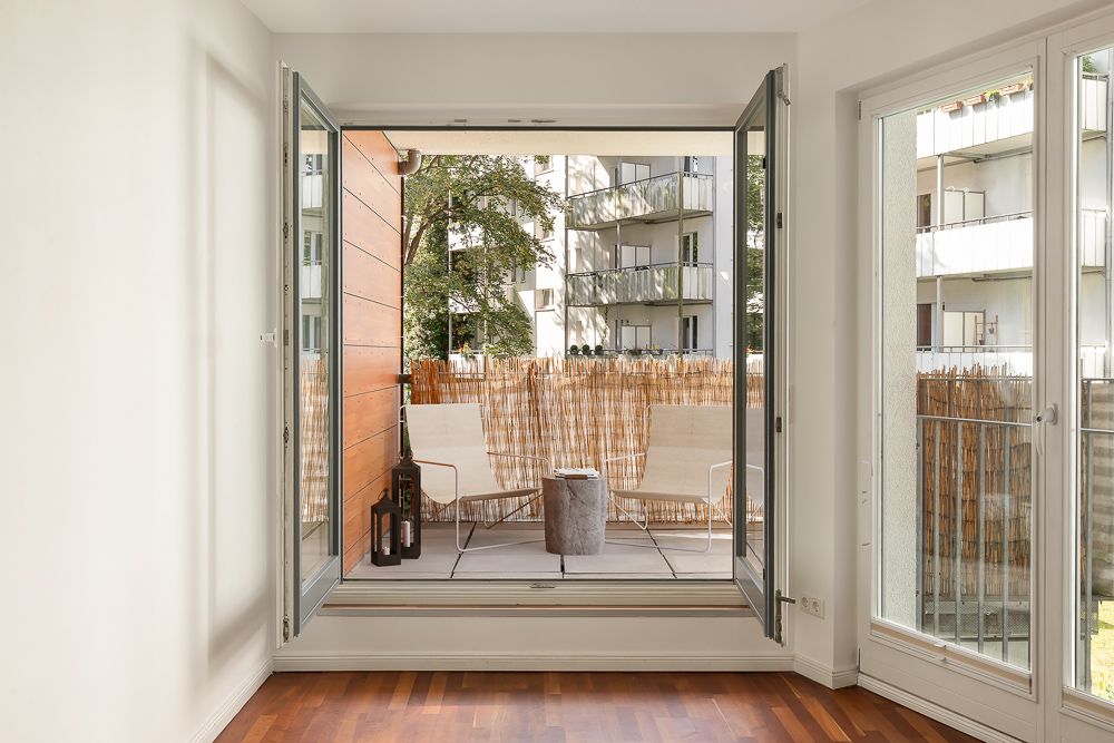 Balkon mit zwei weißen Stühlen, kleinem Tisch und Flaschen, Blick auf Wohngebäude.