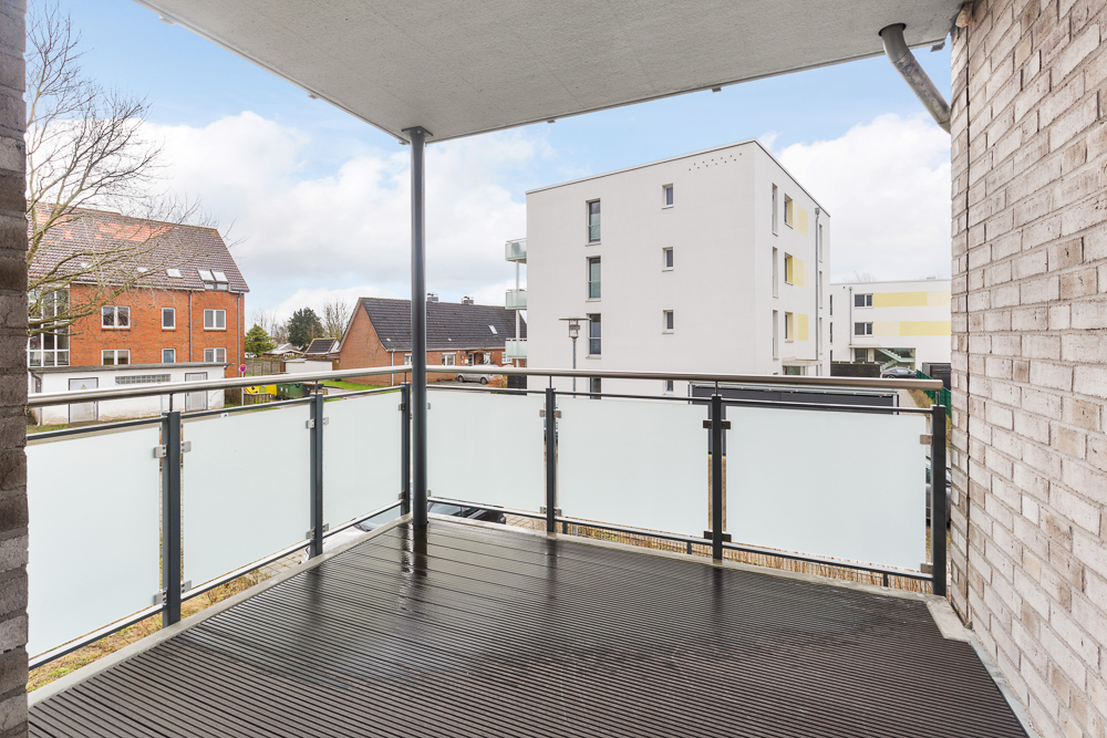 Überdachter Balkon mit Glasgeländer, Blick auf Wohnhäuser und Bäume.