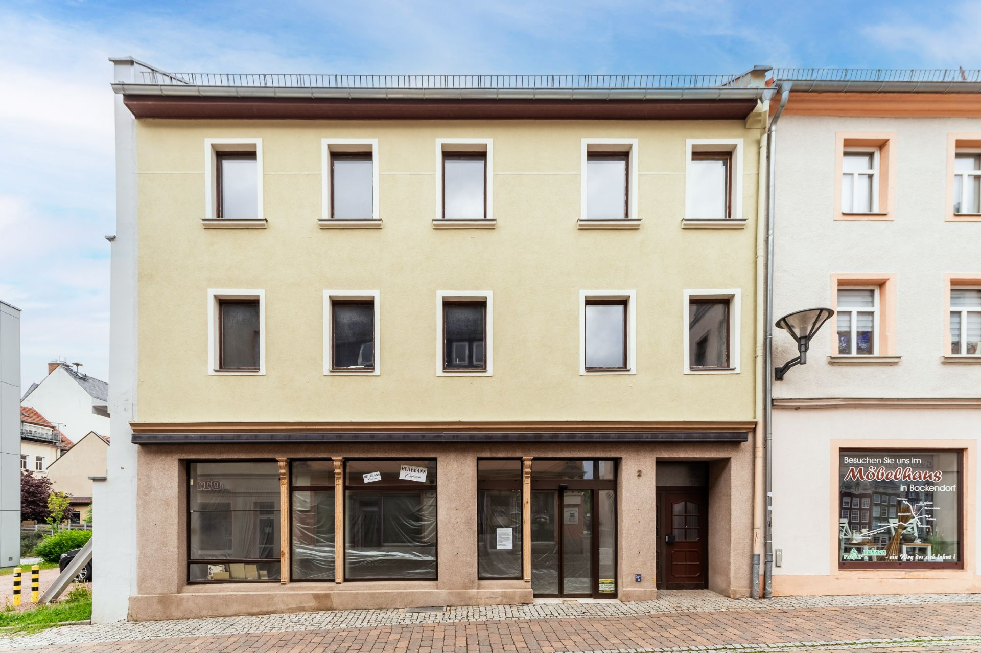 Dreistöckiges Wohnhaus mit sechs Fenstern und zwei Eingängen, gelbe Fassade.