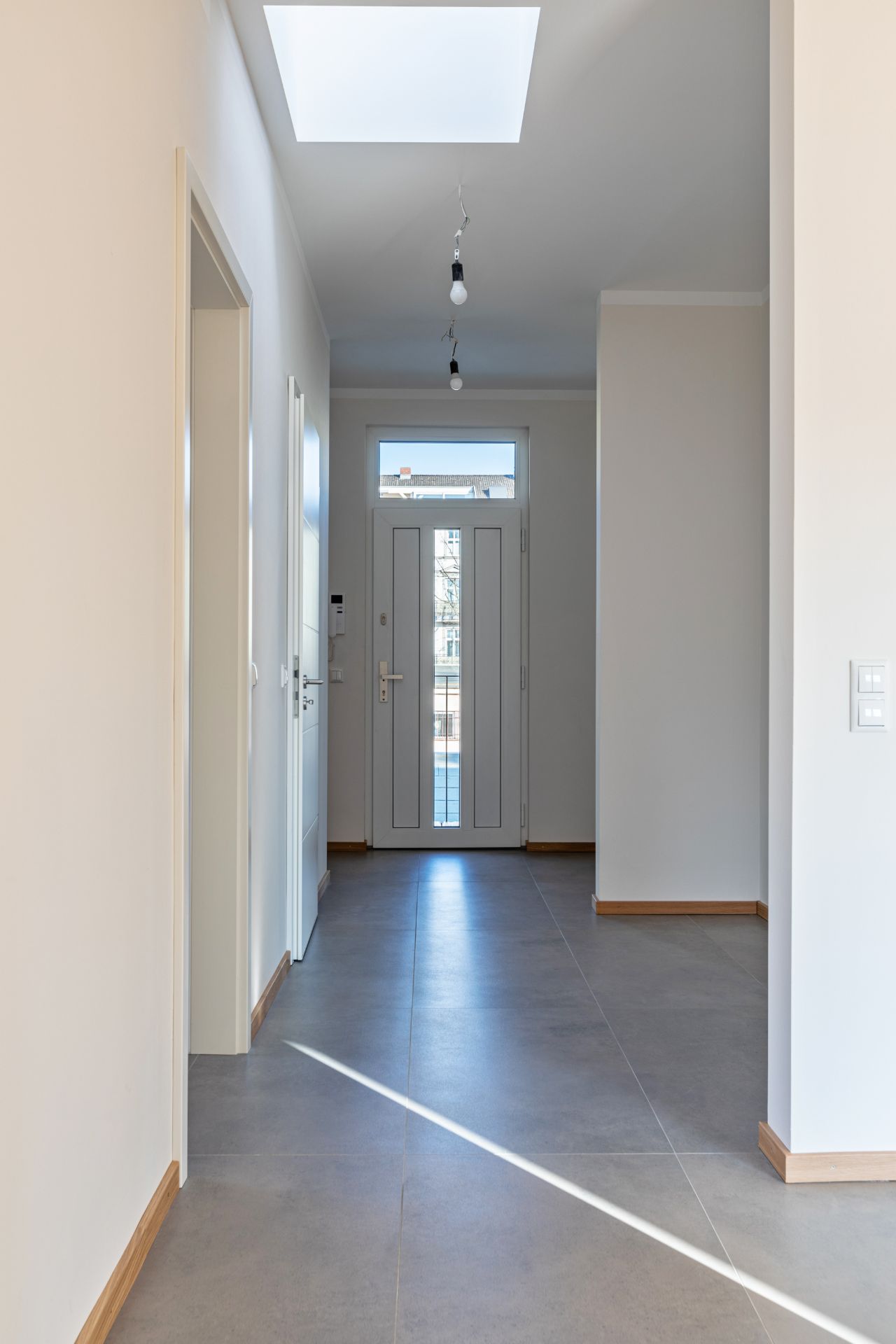 Heller Flur mit grauem Fliesenboden, weißen Wänden und Glastür am Ende.