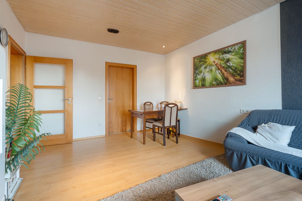 Wohnzimmer mit Holzboden, Tisch, Stühlen, Sofa, Pflanze und Wandbild von Bäumen.