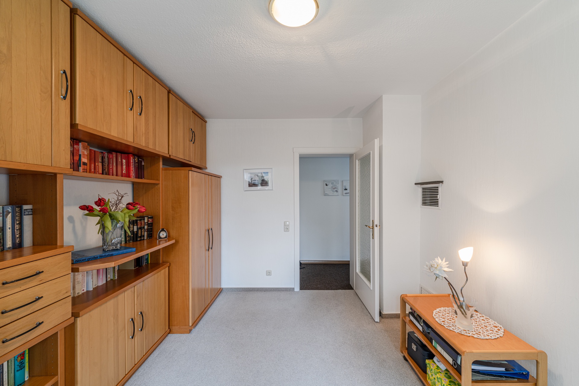 Wohnzimmer mit Holzregal, Bücher, Dekoration und kleinem Tisch mit Lampe.