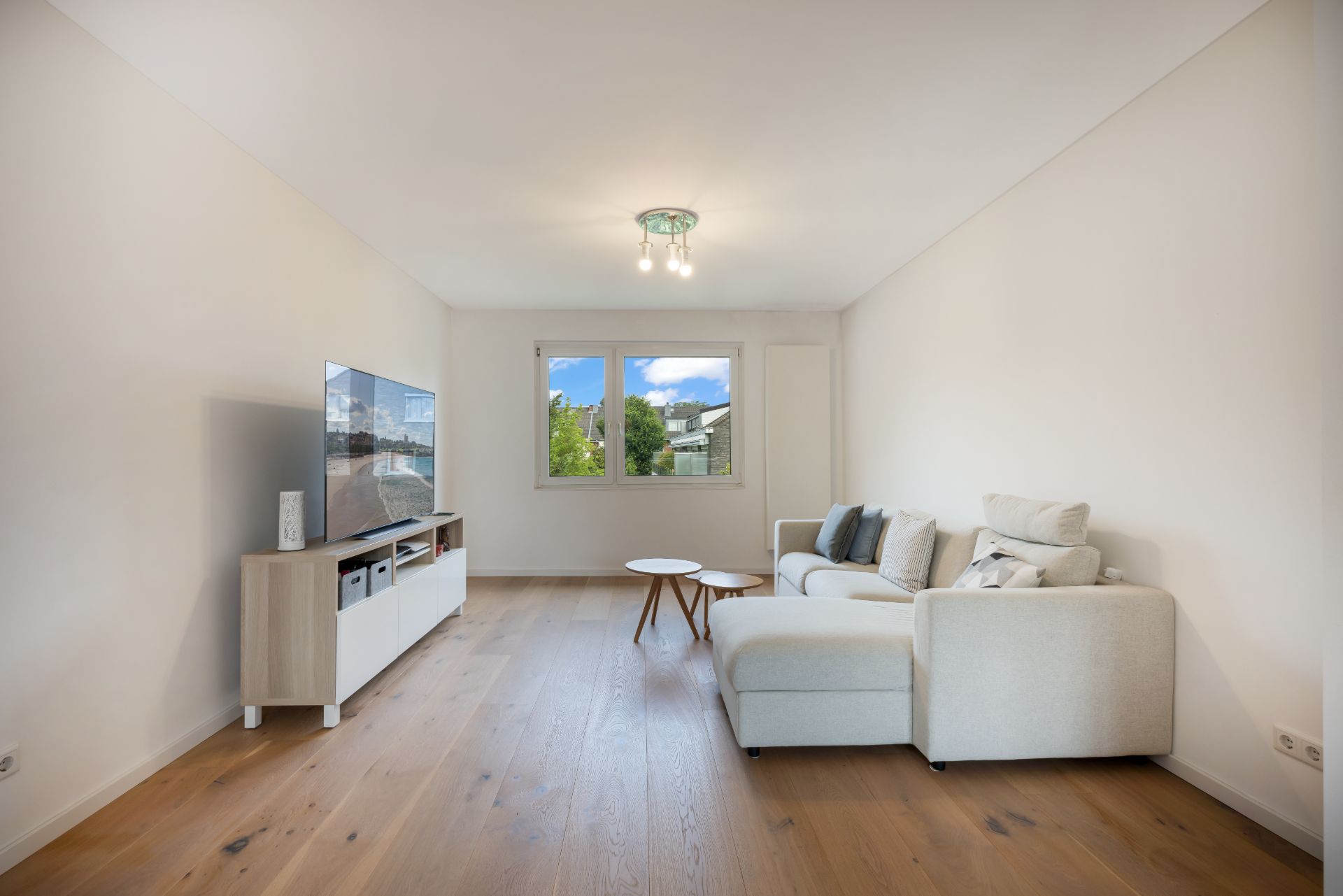Helles Wohnzimmer mit Sofa, TV, Holzboden und großem Fenster mit Ausblick.