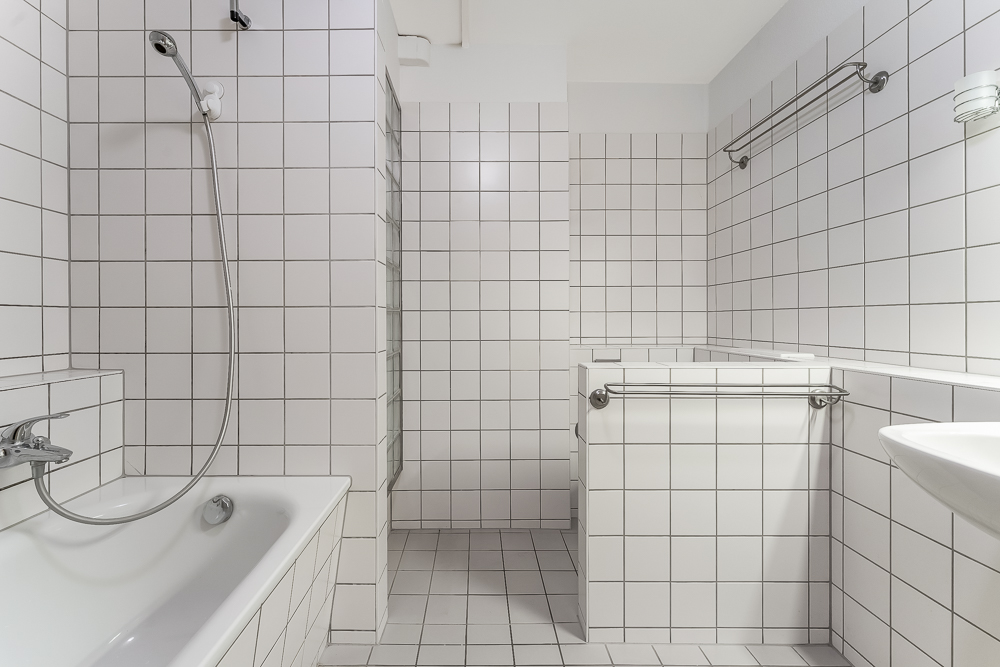 Helles Badezimmer mit weißen Fliesen, Badewanne und Handtuchhaltern.