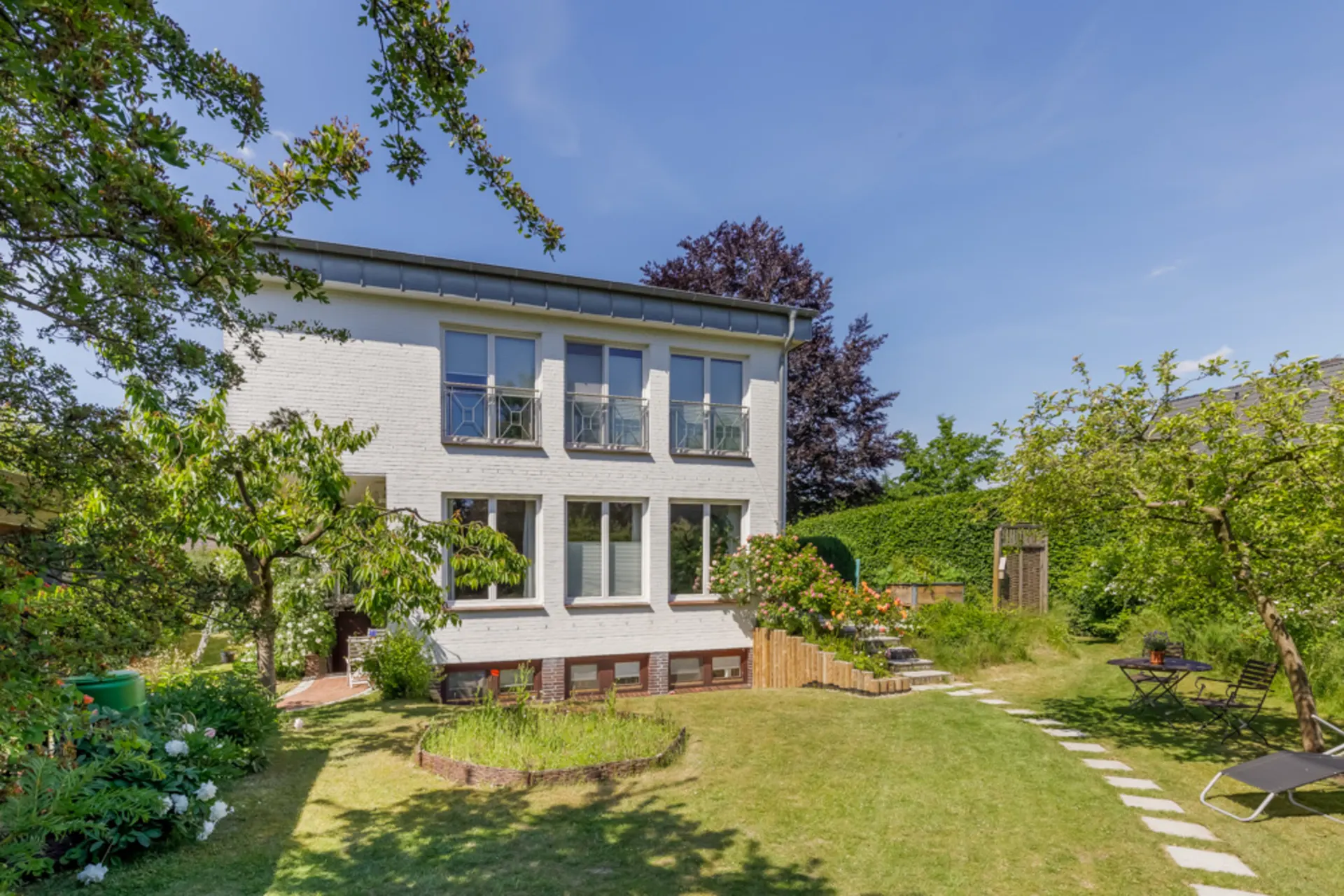 Modernes, weißes Wohnhaus mit großem Garten und Gartenmöbeln an einem sonnigen Tag.