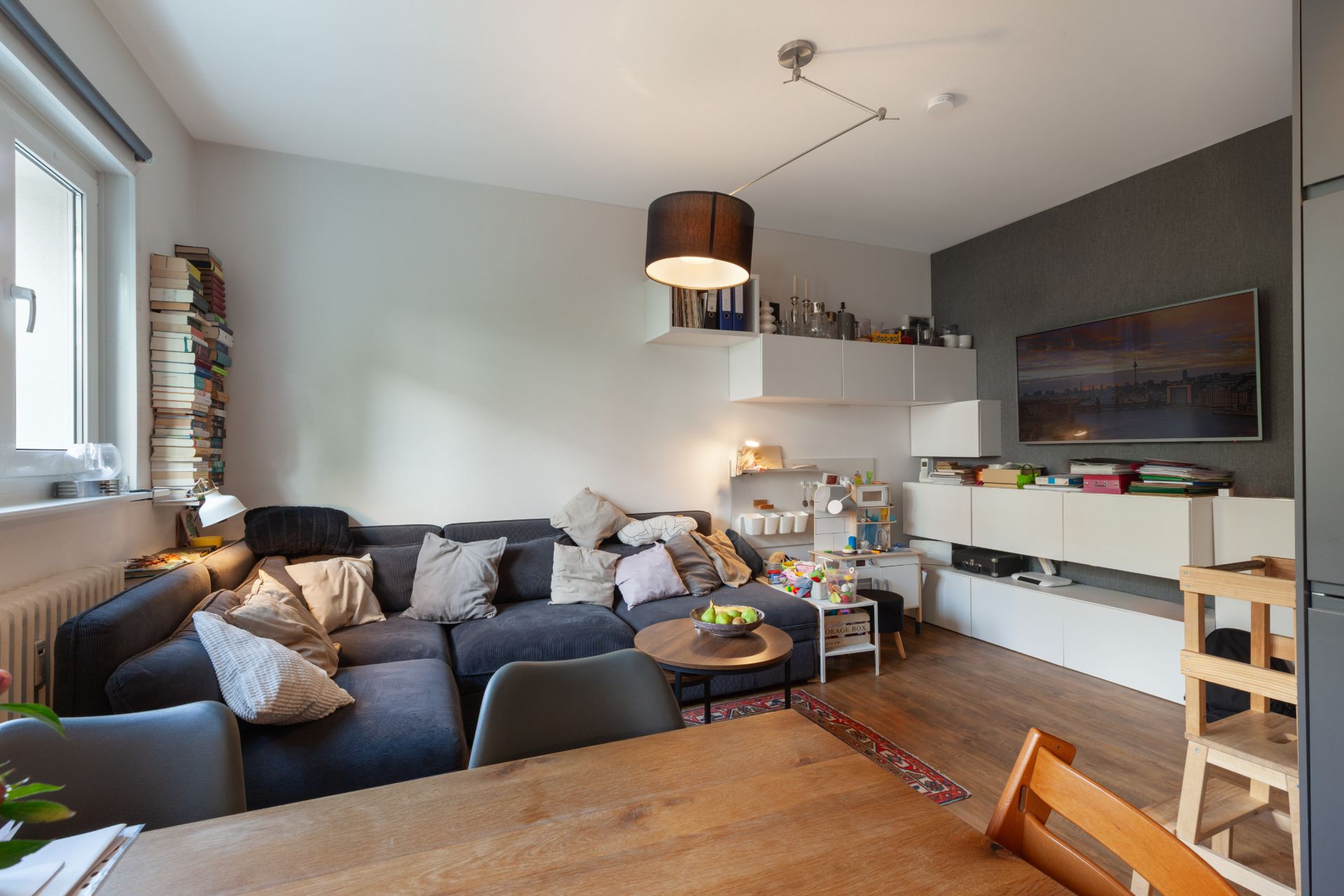 Wohnzimmer mit dunkelblauem Sofa, Couchtisch, Spielzeug und Regalen an der Wand.
