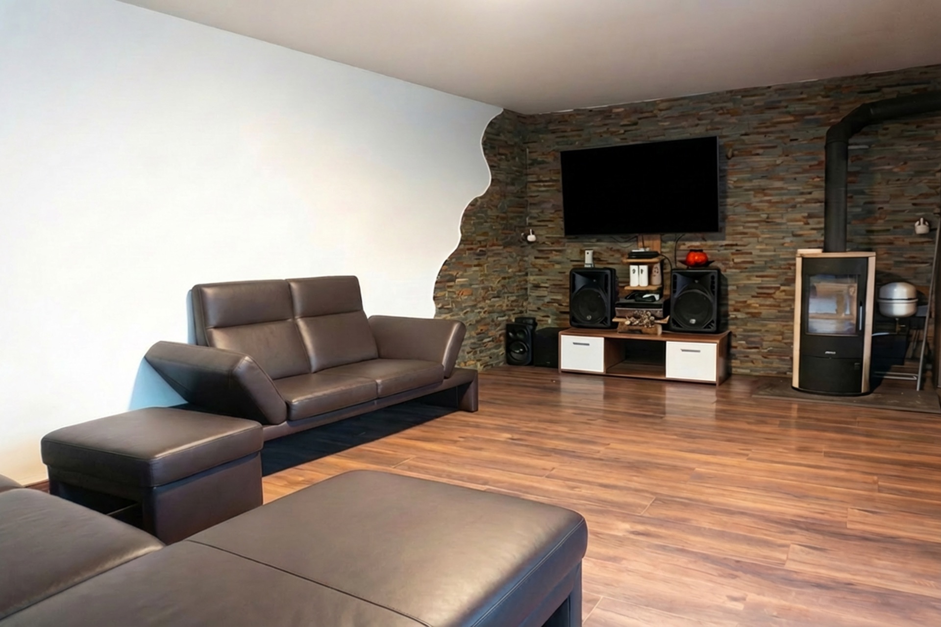 Modernes Wohnzimmer mit braunen Ledersofas, TV, Lautsprechern und Kamin auf Holzfußboden.