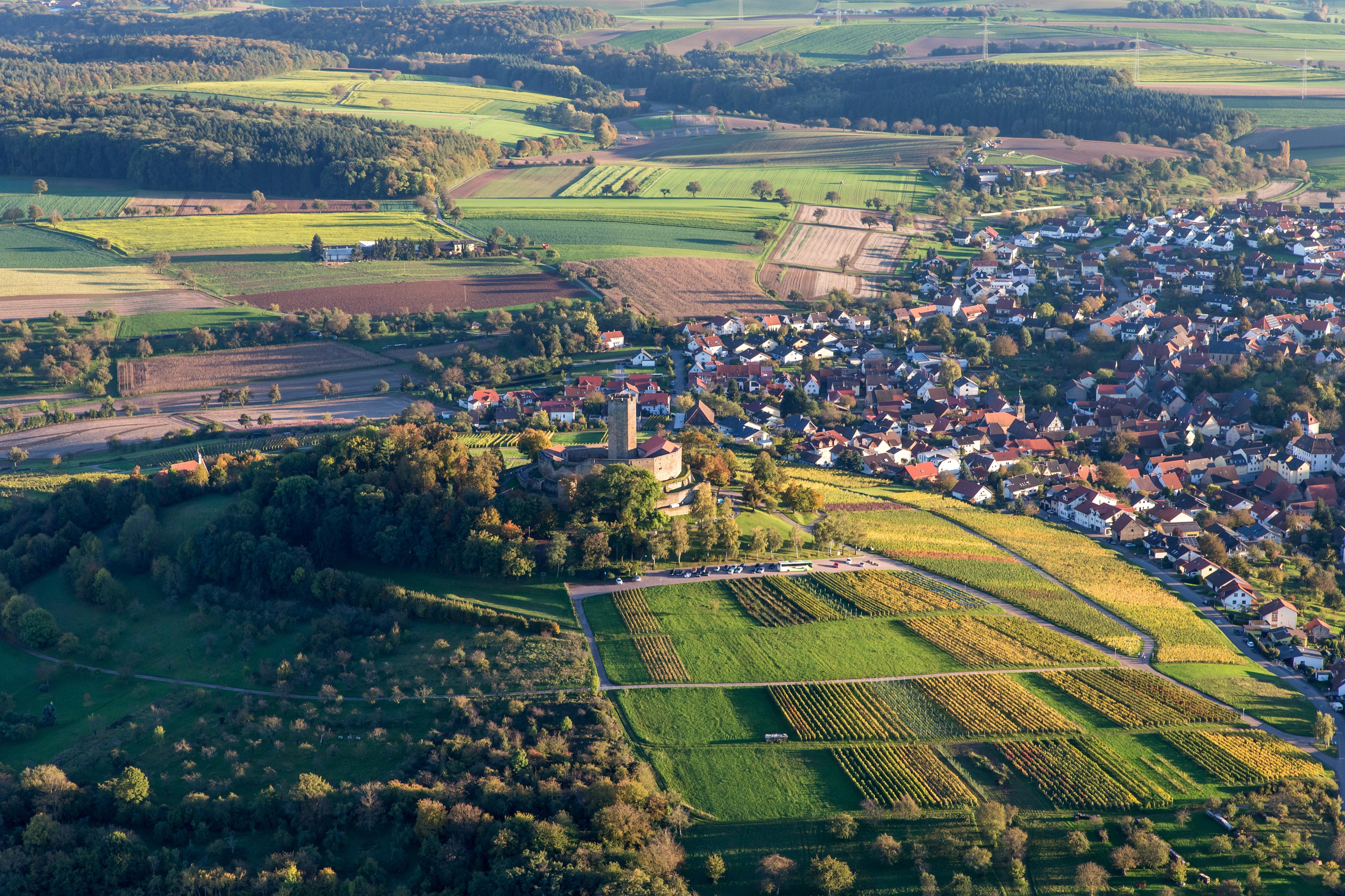 Luftaufnahme eines Dorfes mit Feldern, Wäldern und einem Schloss auf einem Hügel.