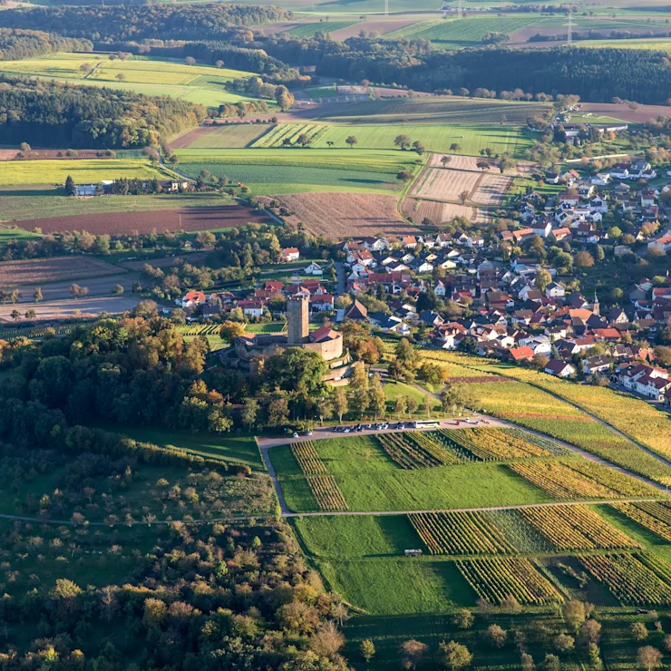 Luftaufnahme eines Dorfes mit Feldern, Wäldern und einem Schloss auf einem Hügel.