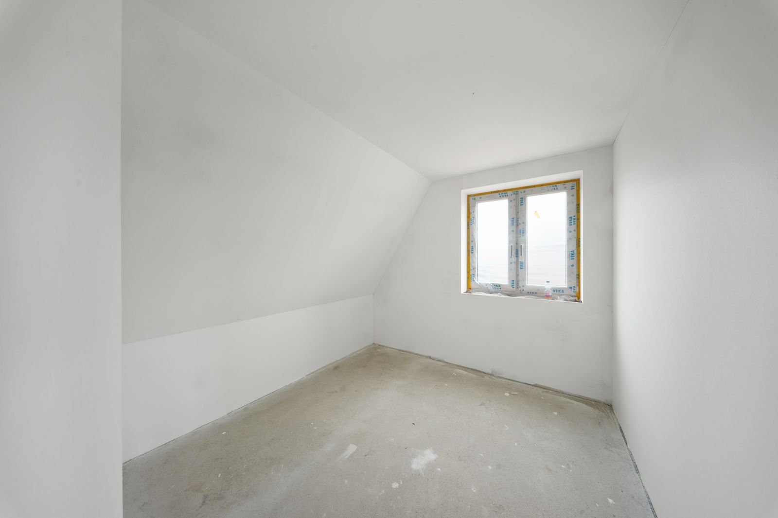 Leerer, weiß gestrichener Raum mit einem Fenster und unfertigem Boden.