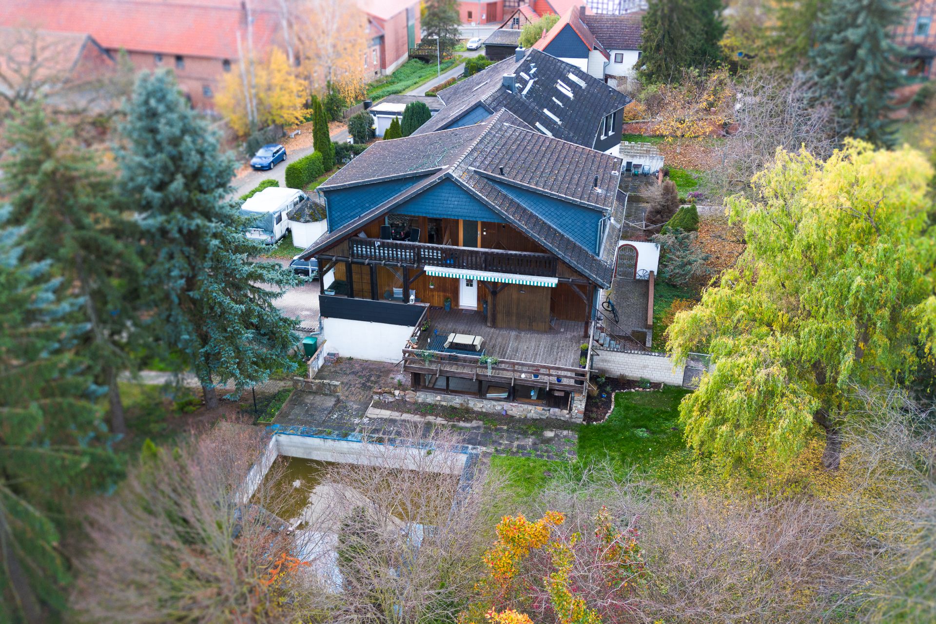 Großes Wohnhaus mit Holzbalkon und Terrasse, umgeben von Bäumen und Garten, aus der Vogelperspektive.