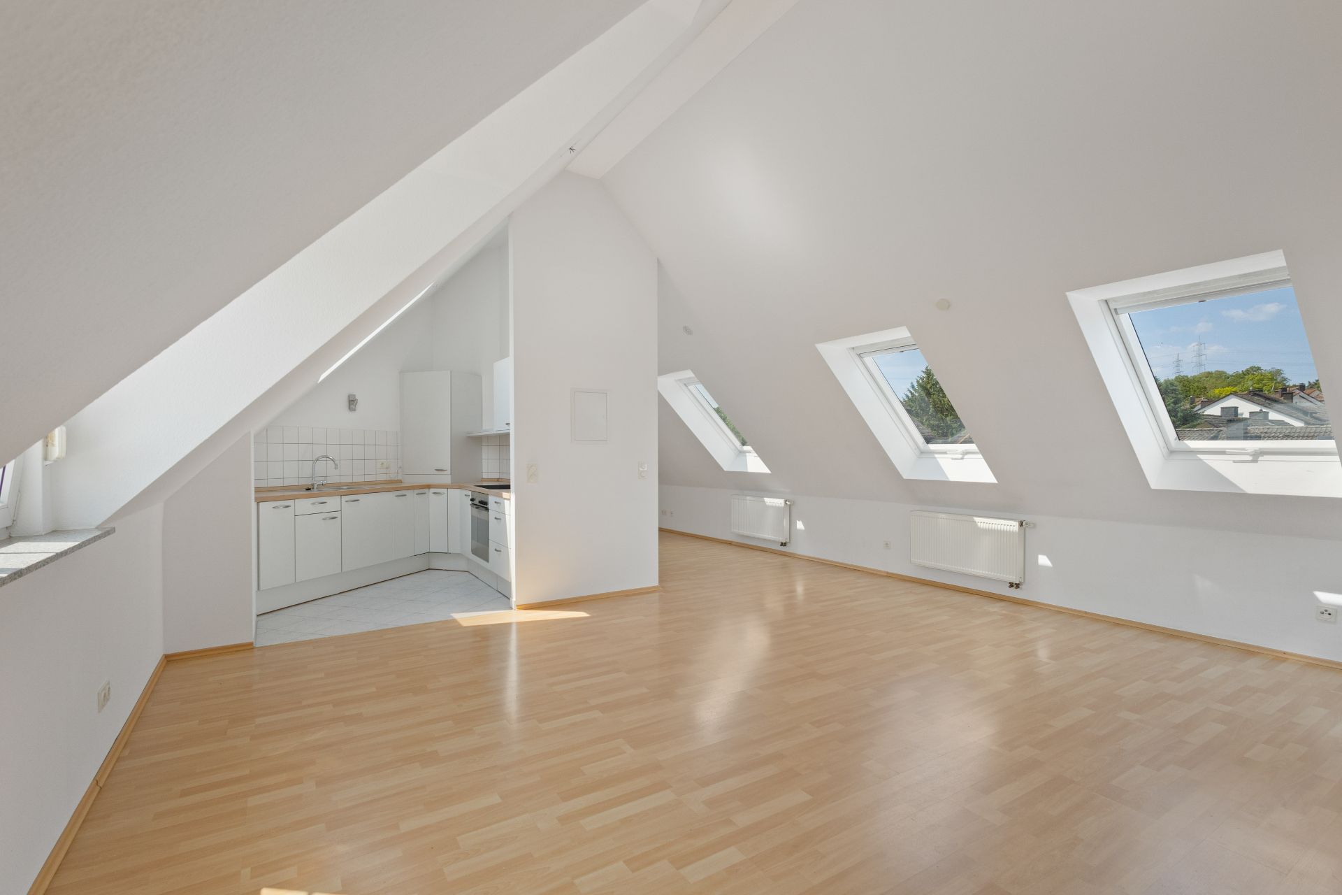 Helles Dachgeschosszimmer mit Einbauküche, Schrägen und mehreren Dachfenstern.