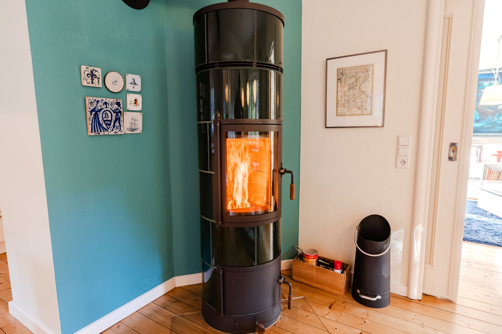 Schwarzer Kaminofen mit Feuer an einer blaugrünen Wand in einem Wohnraum.