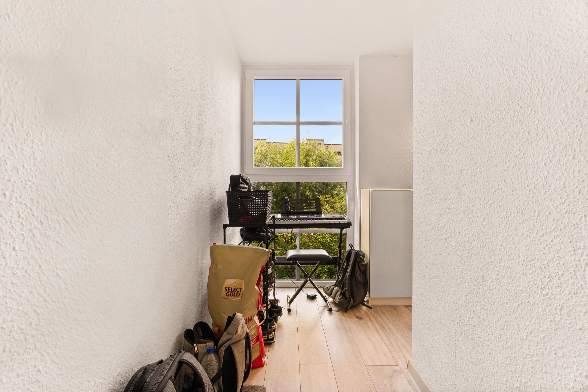 Kleiner Raum mit Fenster, Keyboard auf einem Tisch und mehreren Rucksäcken am Boden.
