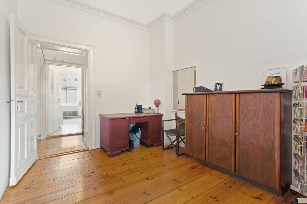 Raum mit Holzboden, Schreibtisch, Stuhl und großem Holzschrank, Tür führt in einen anderen Raum.