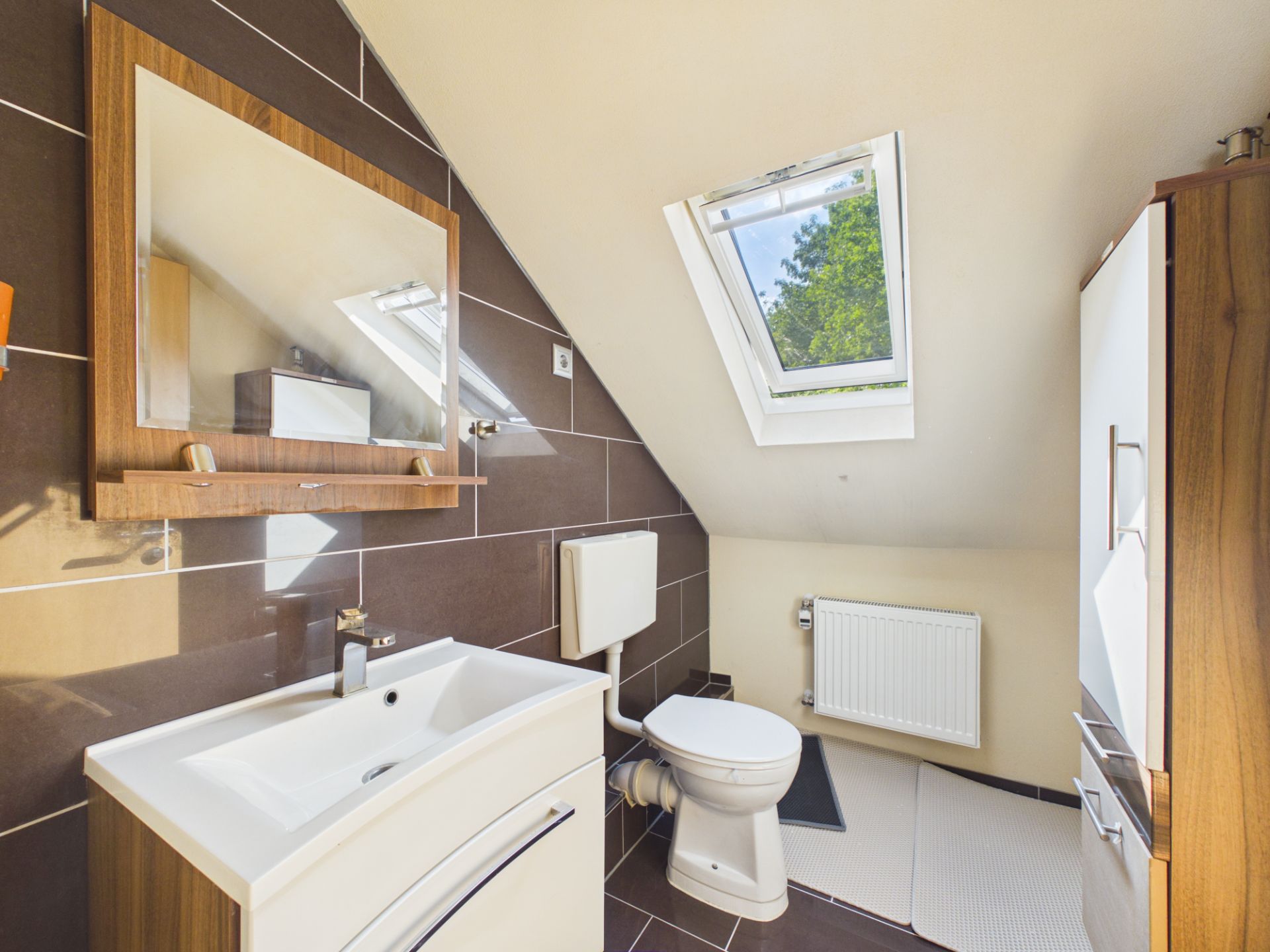 Modernes Bad mit Waschbecken, Toilette, Spiegel und Dachfenster unter einer Schräge.