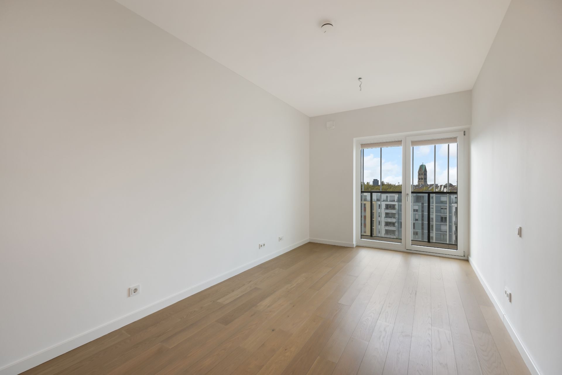 Leeres Zimmer mit Holzboden und bodentiefen Fenstern, Blick auf Stadtgebäude.