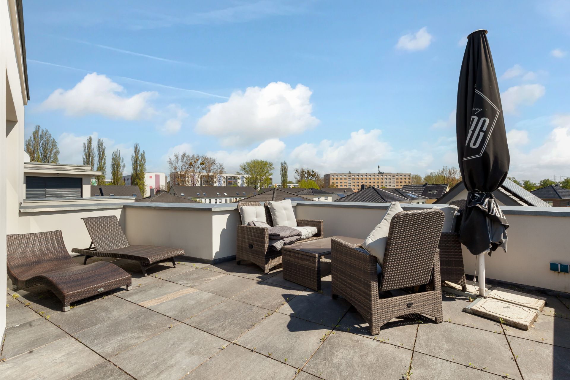 Geräumige Dachterrasse mit Sitzmöbeln, Sonnenschirm und Ausblick auf Nachbargebäude bei Tageslicht.