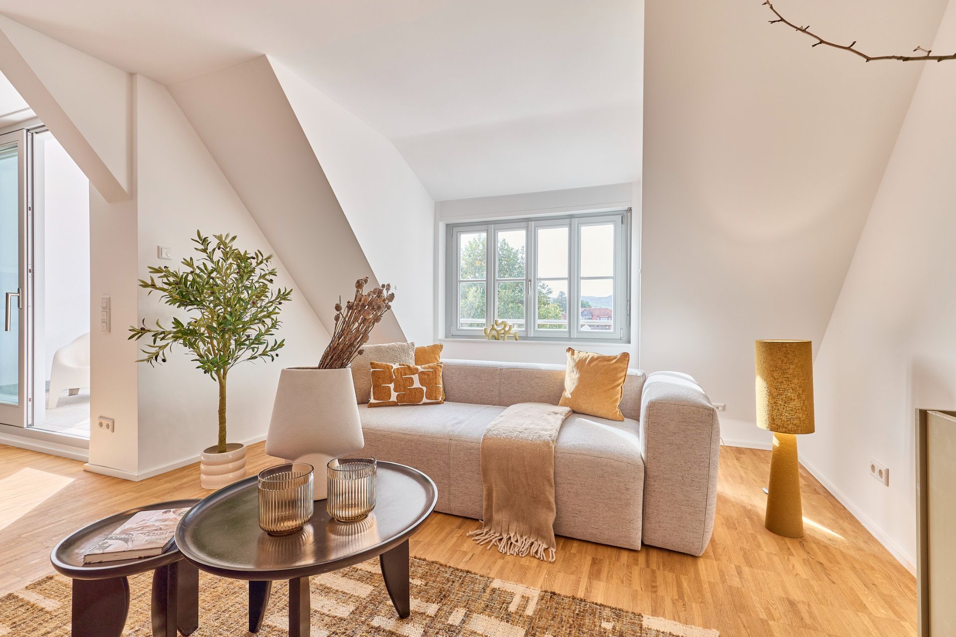 Modernes Wohnzimmer mit grauem Sofa, Holztisch, Zimmerpflanze und großem Fenster.