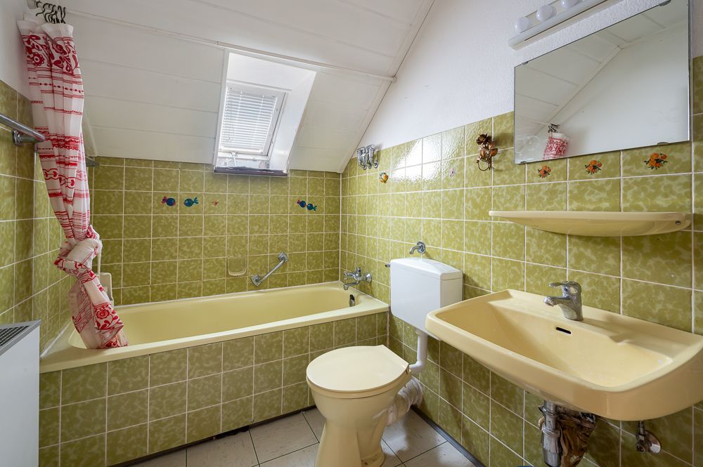 Badezimmer mit gelben Fliesen, Badewanne, Waschbecken, Toilette und kleinem Fenster im Dach.