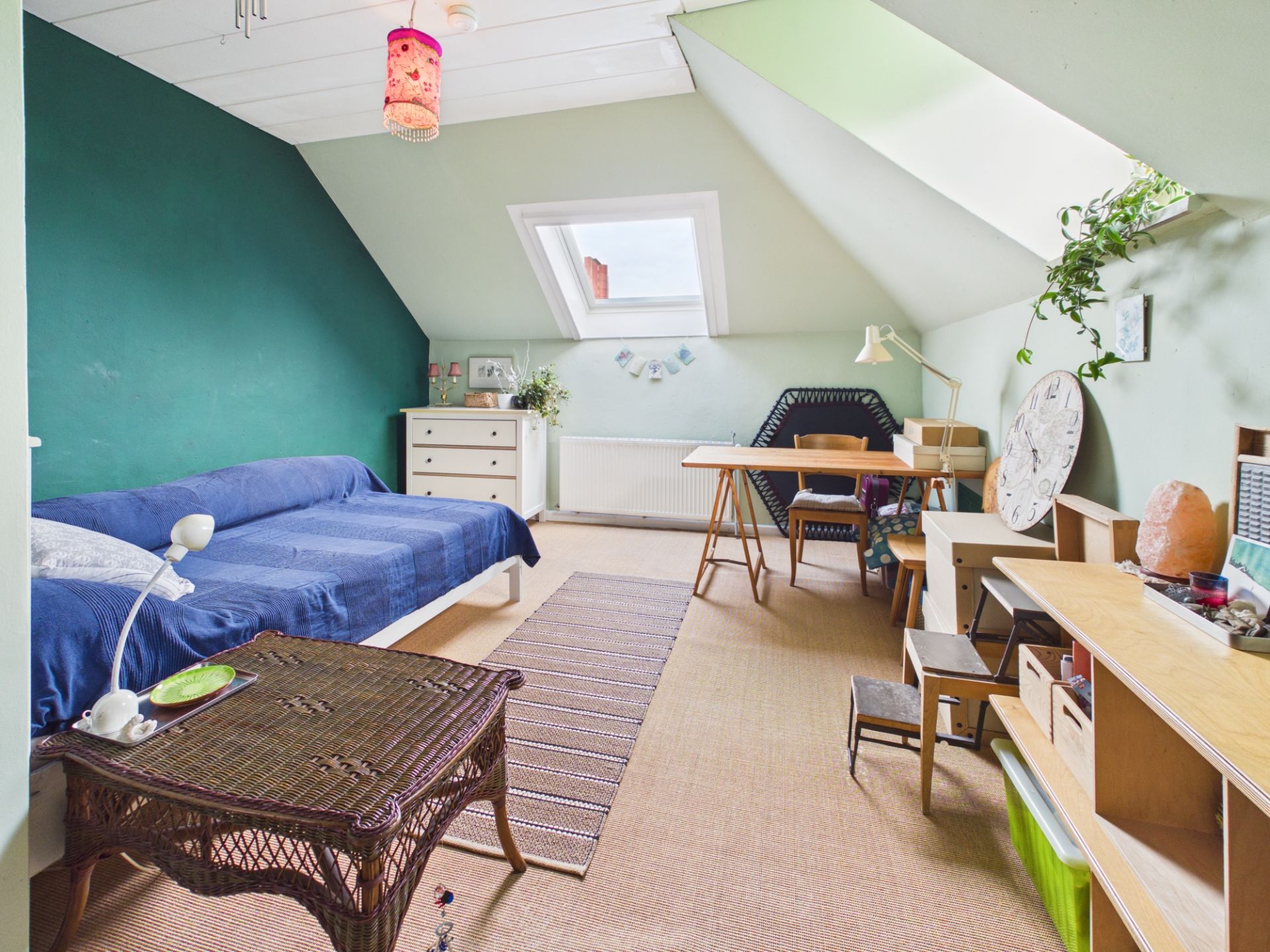Helles Dachzimmer mit Bett, Schreibtisch, Regal und Dachfenster.
