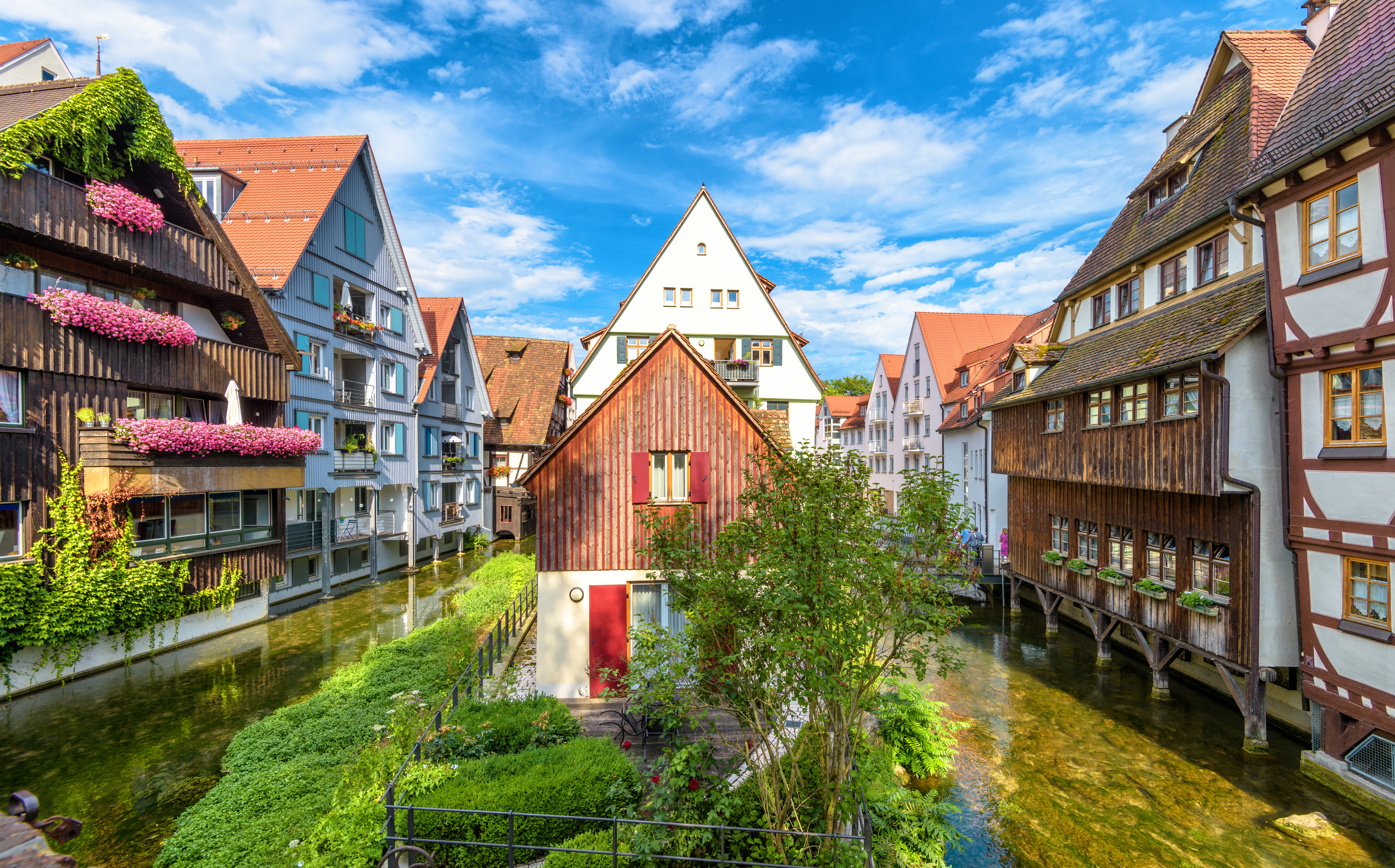 Traditionelle Fachwerkhäuser an einem klaren Kanal mit bunten Blumen an den Balkonen.