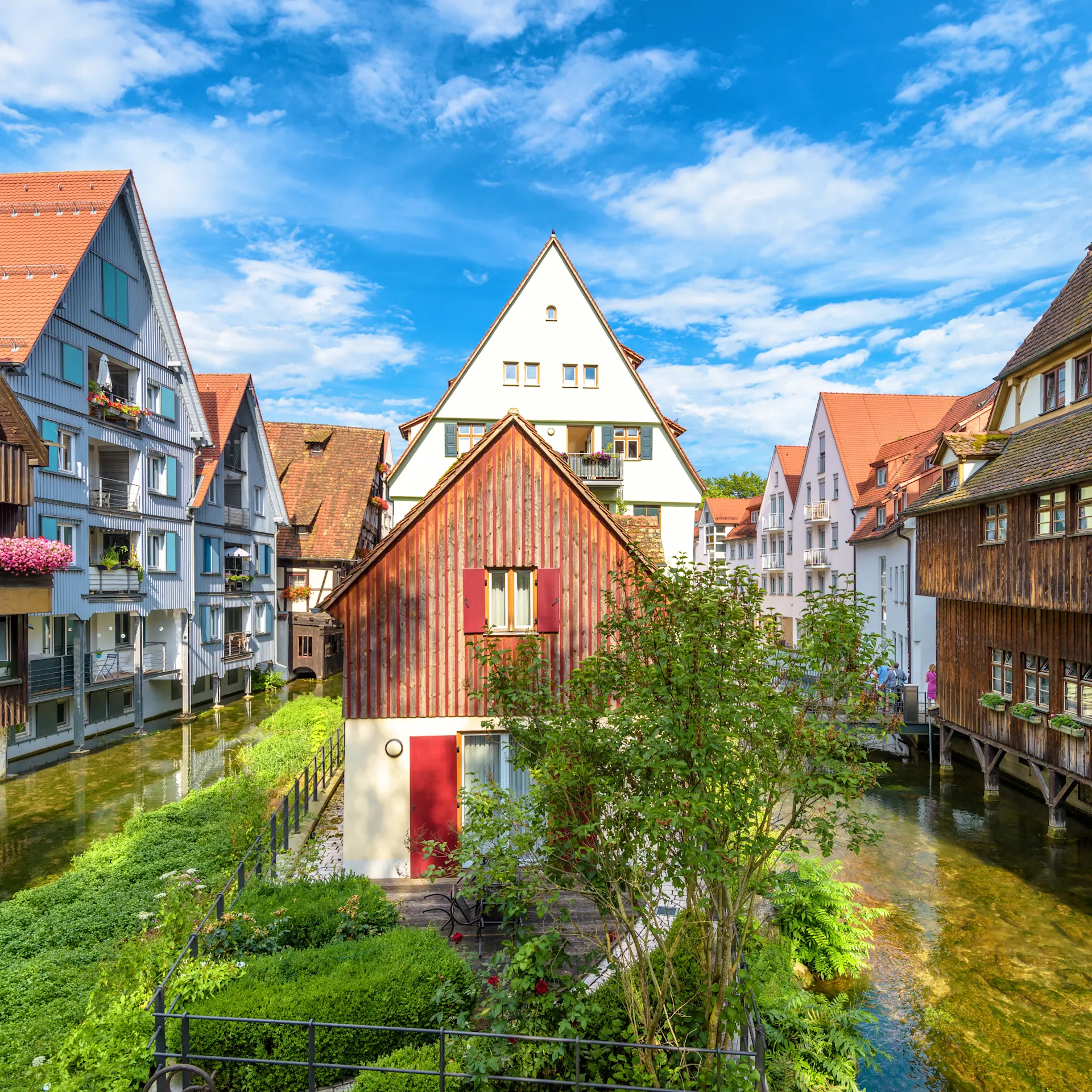 Traditionelle Fachwerkhäuser an einem klaren Kanal mit bunten Blumen an den Balkonen.