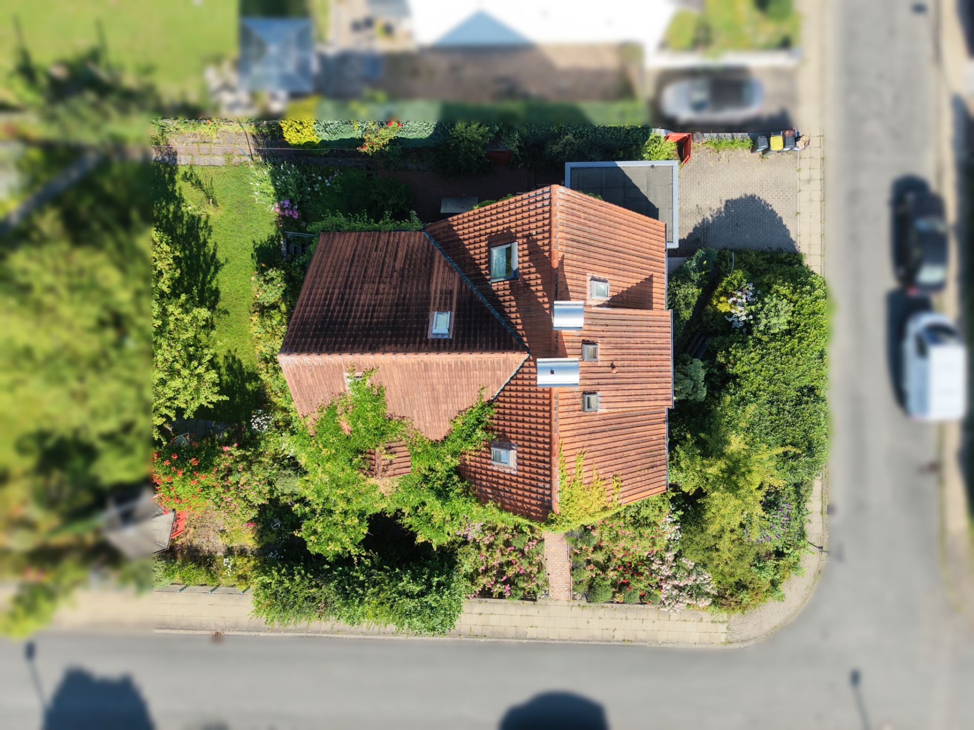 Luftbild eines Hauses mit rotem Dach, umgeben von Grünflächen und Straßen.