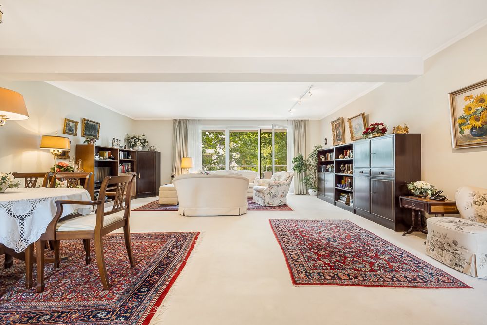 Geräumiges Wohnzimmer mit Sofas, Teppichen, Regalen und großem Fenster mit Blick ins Grüne.