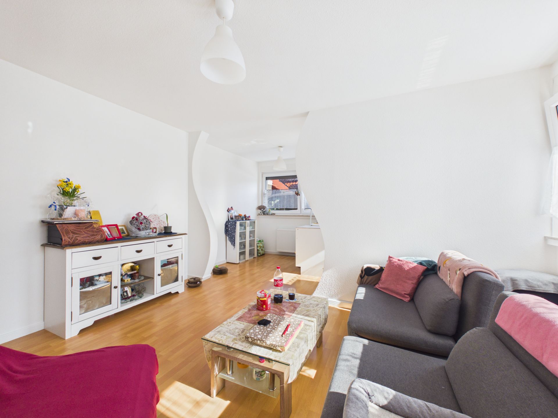 Helles Wohnzimmer mit grauem Sofa, Couchtisch und Sideboard auf Holzfußboden.