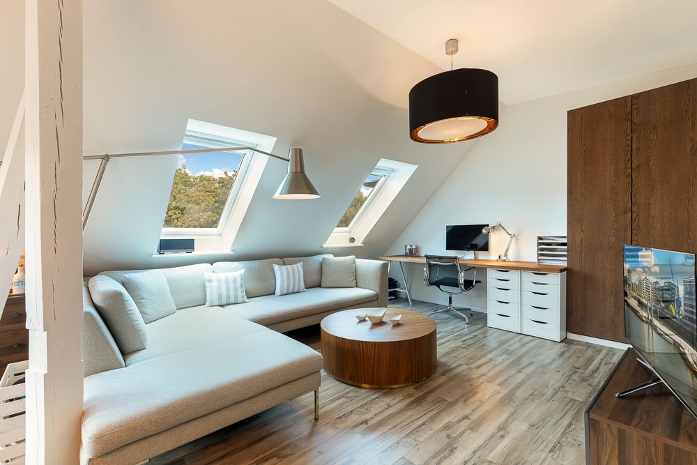 Modernes Wohnzimmer mit Ecksofa, Couchtisch, Schreibtisch und zwei Dachfenstern.