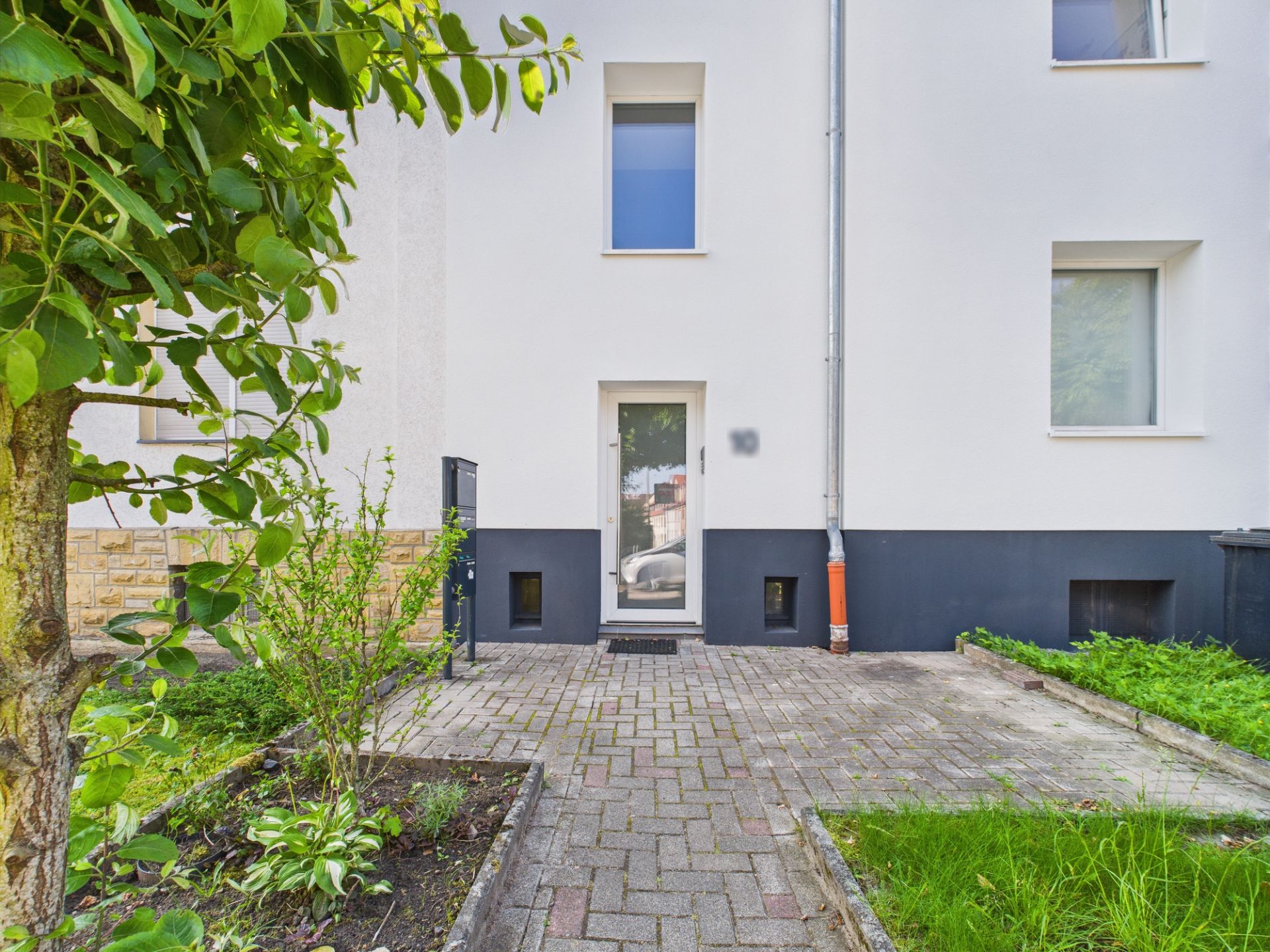 Eingang eines Wohnhauses mit gepflastertem Weg und kleinem Garten.