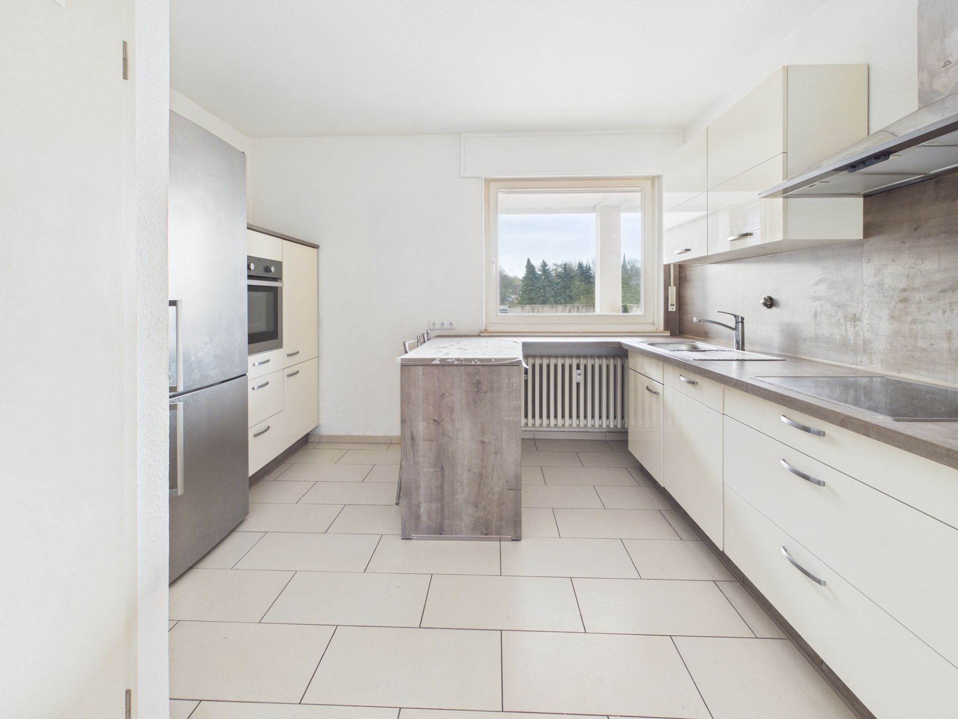 Helle, moderne Küche mit Kücheninsel, großen Fenstern und weißen Schränken.