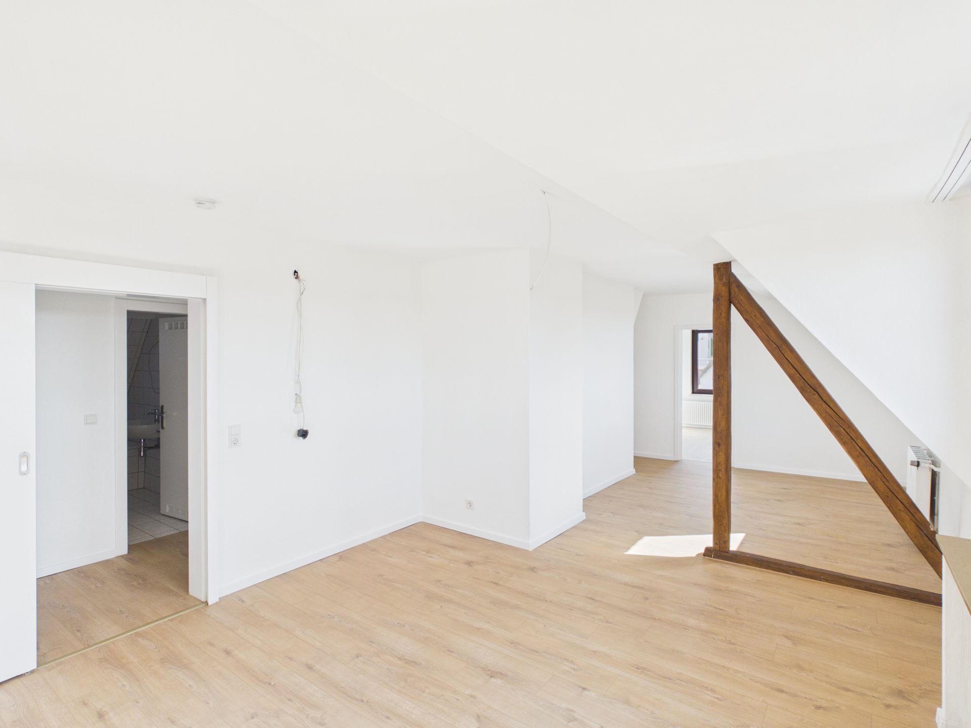 Heller Raum mit Holzfußboden, weißen Wänden und sichtbarem Holzbalken.